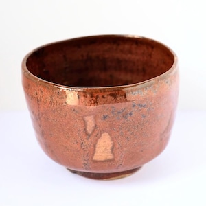 May include: A handcrafted ceramic bowl with a textured, rustic finish. The bowl features a reddish-brown glaze with copper-toned highlights. The interior is a darker brown. This bowl is suitable for serving or decorative purposes.