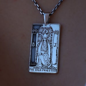 Könnte beinhalten: Eine silberne Kettenkette mit einem Anhänger, der eine Schwarzweißillustration der Tarotkarte Die Hohepriesterin zeigt.