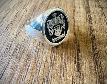 May include: A silver signet ring with a black enamel crest featuring a coat of arms and the text "Del Rio".