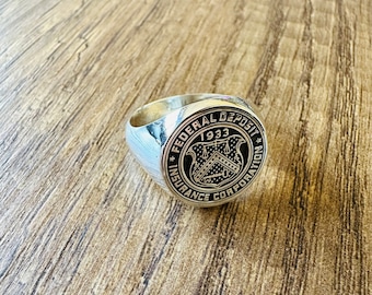 May include: A silver ring with a black and gold emblem that reads "Federal Deposit Insurance Corporation 1933".
