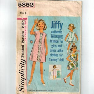 Op de afbeelding: Vintage Simplicity patroon voor Jiffy Tammy poppenkleding, maat 6. Het patroon bevat illustraties van jurken, waaronder een roze ruitjesjurk met bloemenrand. Het patroon komt uit 1962.