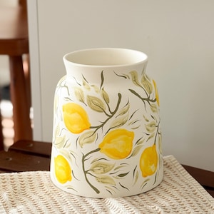 May include: White ceramic vase with a hand-painted design of yellow lemons and green leaves.