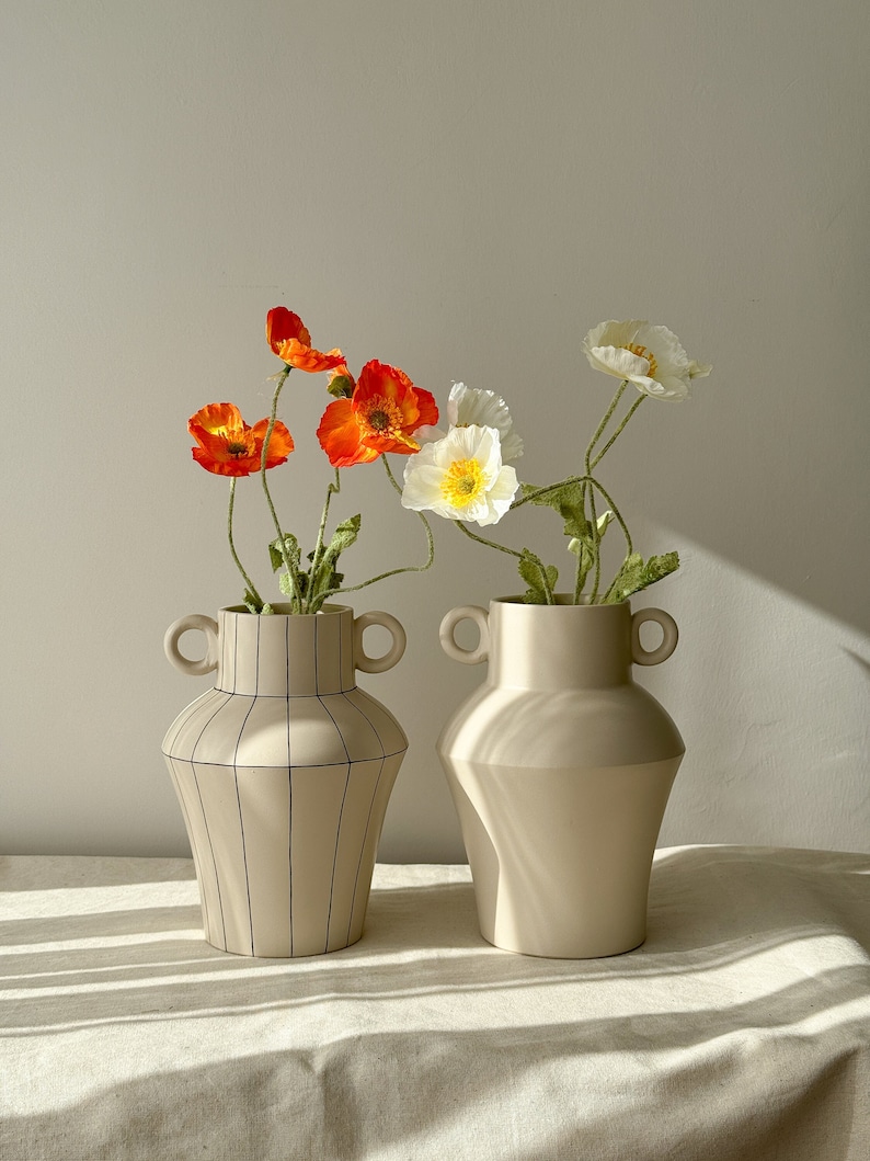 There are two vases. One is a plain cream color. The other one is cream colored and has a striped pattern.