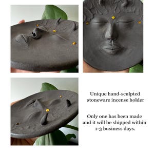 May include: Black stoneware incense holder shaped like a face with closed eyes and a small mouth. The holder has gold accents around the eyes and mouth.