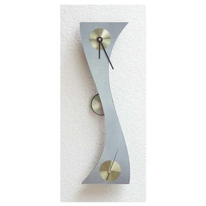 May include: A modern wall clock with a silver-colored, curved frame and two gold-colored clock faces. The clock hands are black.