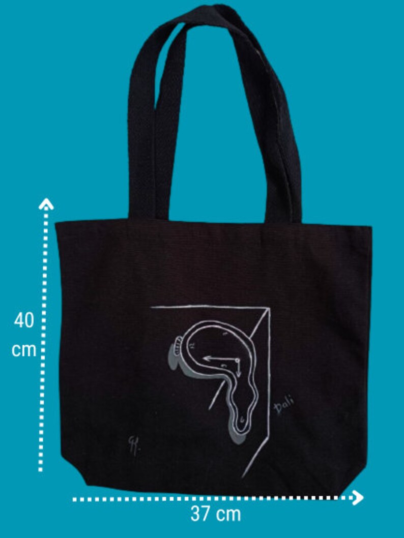 May include: Black canvas tote bag featuring a white illustration of a melting clock and the word "Dali" on the front. The bag measures 37 cm wide and 40 cm tall.