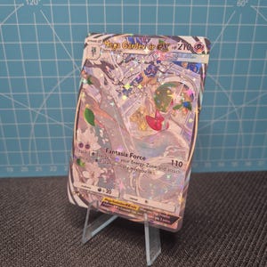 May include: A holographic Mega Gardevoir EX trading card, displayed on a clear acrylic stand. The card features a detailed illustration with a white, pink, and green color scheme. Text includes "Fantasia Force" and "HP 270".