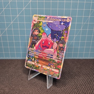 May include: A Team Rocket's Tinkaton trading card with 140 HP, featuring a holographic finish and a colorful illustration of the character holding a large hammer. The card displays the Pile-Driving Hammer attack text and various game statistics.