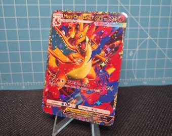 Puede incluir: Una carta coleccionable Pokémon Mega Charizard Y EX. La carta presenta una vibrante ilustración de Charizard en tonos naranja, rojo y azul. La carta muestra el texto "Crimson Dive" y "250". La carta se muestra en un soporte de plástico transparente.