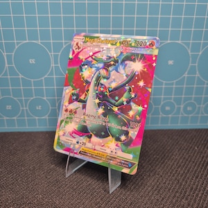 Könnte beinhalten: Eine Pokémon-Sammelkarte von Mega Charizard EX mit dem Text "Raging Blaze" und "220". Die Karte wird auf einem transparenten Kunststoffständer präsentiert. Die Illustration der Karte ist lebendig und farbenfroh.