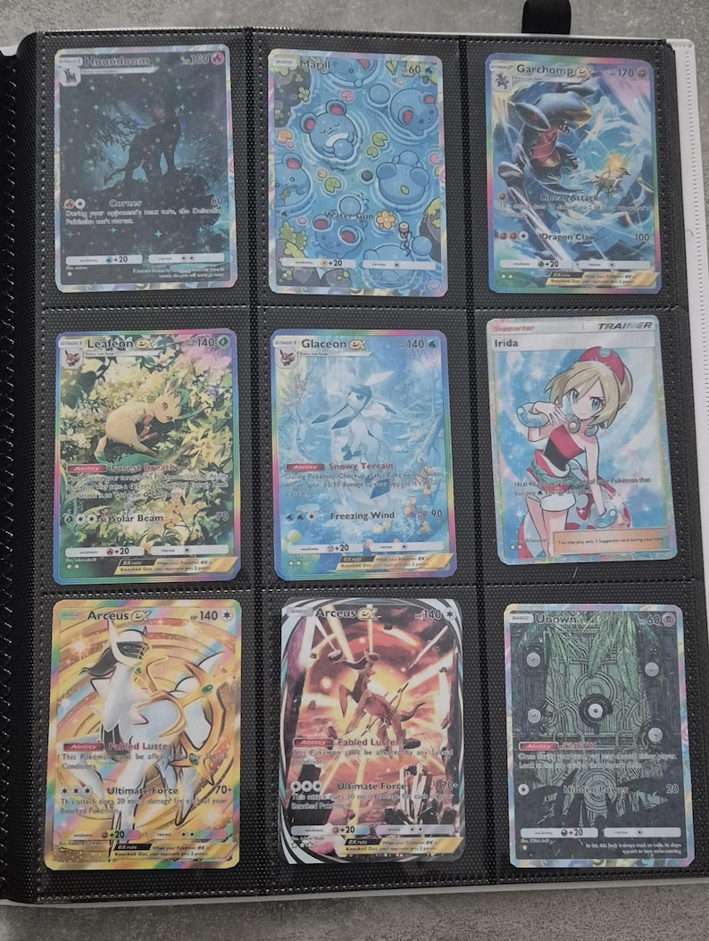 K&ouml;nnte beinhalten: Neun Pok&eacute;mon-Sammelkarten in einem Ordner. Die Karten zeigen verschiedene Charaktere und Designs, darunter Arceus, Garchomp und Glaceon. Die Karten befinden sich in Schutzh&uuml;llen, und der Ordner ist schwarz.