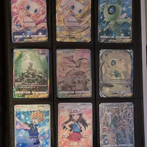 K&ouml;nnte beinhalten: Neun Pok&eacute;mon-Sammelkarten in einem schwarzen Ordner. Die Karten zeigen verschiedene Charaktere, darunter Mew, Celebi und Aerodactyl, mit holografischen und Folienakzenten. Jede Karte hat einen Charakternamen, KP und Angriffsdetails.