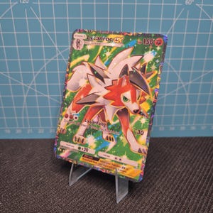 May include: A holographic Lycanroc EX Pokémon trading card. The card features a colorful illustration of a wolf-like creature with red, white, and black fur. The card has text that reads "Lycanroc EX" and "Lycanfang".