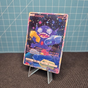 May include: A holographic Sableye trading card featuring a dark purple creature with large gem-like eyes, holding a yellow and a blue crystal. The background is a starry night sky with pink and blue accents. The card displays the text Bubble Beam.