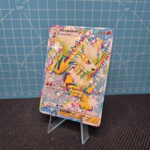 May include: A holographic Arcanine EX Pokémon trading card, displayed on a clear acrylic stand. The card features a colorful illustration of Arcanine with the text "Inferno Onrush" and "HP 150". The card is approximately 3.5 inches tall.