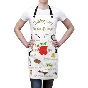 Puede incluir: Delantal blanco con un gráfico de manzana roja y el texto "Cooking with Jessica Fletcher" y varios otros gráficos y textos relacionados con la cocina y la comida.