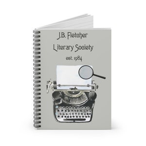 May include: A gray spiral notebook with the text "J.B. Fletcher Literary Society est. 1984" and a watercolor illustration of a vintage typewriter with a magnifying glass.
