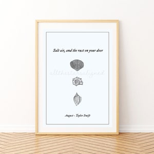 May include: A framed print with a white background and black text that reads "Salt air, and the rust on your door" with three black and white illustrations of seashells. The text "August - Taylor Swift" is at the bottom of the print.