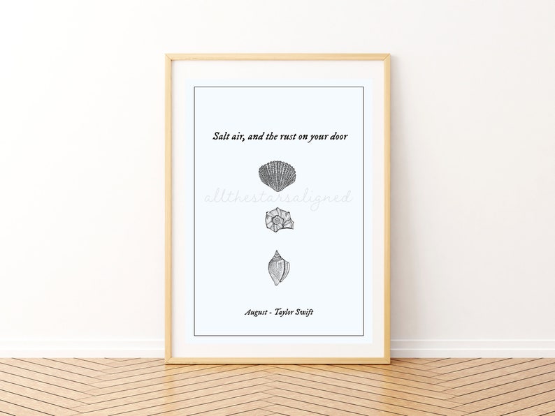 May include: A framed print with a white background and black text that reads "Salt air, and the rust on your door" with three black and white illustrations of seashells. The text "August - Taylor Swift" is at the bottom of the print.