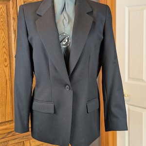 May include: A black blazer with a classic design. The blazer features a notched lapel, a single-button closure, and two front pockets. The garment is displayed on a mannequin. The blazer is a versatile piece of clothing.