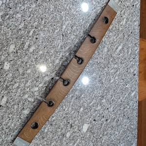 May include: A wooden coat rack made from a repurposed barrel stave. It features three black metal hooks and metal end caps. The wood has a natural grain and is stained a medium brown color.