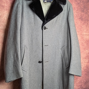 May include: A gray coat featuring a black faux fur collar, a button-front closure, and two side pockets. The interior label reads Pendleton, and the garment is displayed on a black hanger against a textured, mottled reddish-brown background.