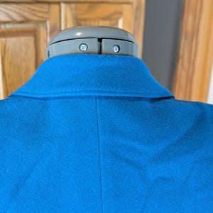 May include: A close-up of a bright blue blazer, showcasing the collar and back. The fabric appears to be a soft wool or wool blend. The blazer is displayed on a mannequin with a gray head.