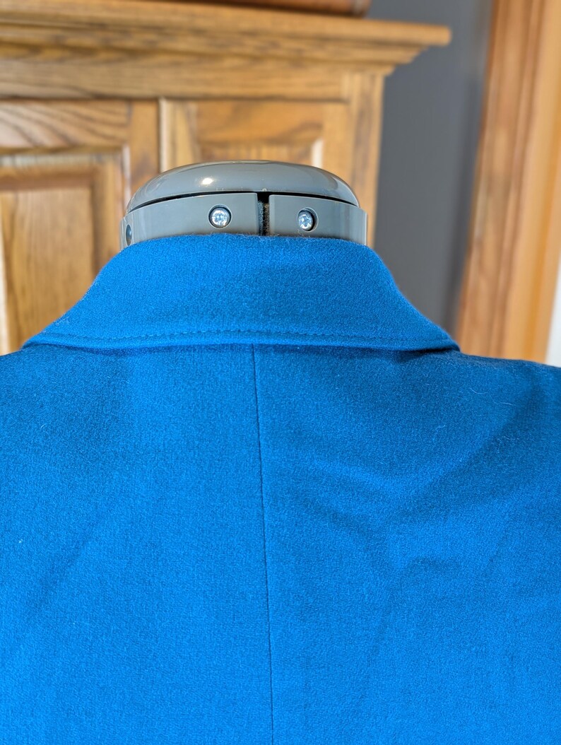 May include: A close-up of a bright blue blazer, showcasing the collar and back. The fabric appears to be a soft wool or wool blend. The blazer is displayed on a mannequin with a gray head.