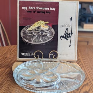 May include: A clear glass egg hors d'oeuvre serving tray with a leaf design. The tray is 13 inches in diameter and comes with its original box. The box reads "egg hors d'oeuvre tray one 13" serving tray".
