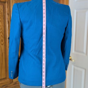 May include: A bright blue blazer with a three-button closure on the sleeve. A pink measuring tape shows the blazer's length is approximately 28 inches. The blazer is displayed on a mannequin.