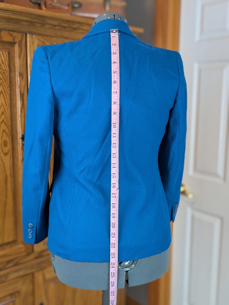 May include: A bright blue blazer with a three-button closure on the sleeve. A pink measuring tape shows the blazer's length is approximately 28 inches. The blazer is displayed on a mannequin.