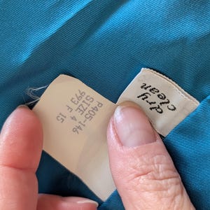 May include: Close-up of a teal fabric with two tags. One tag reads "Dry Clean" in black text. The other tag has the text "P405-146 SIZE 4 993 F 15".