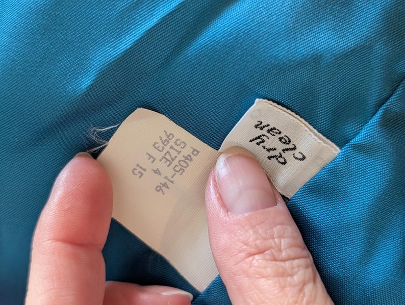 May include: Close-up of a teal fabric with two tags. One tag reads "Dry Clean" in black text. The other tag has the text "P405-146 SIZE 4 993 F 15".