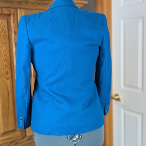 May include: A bright blue blazer displayed on a dress form. The blazer has a classic tailored design with a notched lapel and three buttons on each cuff. The back view shows a fitted silhouette.