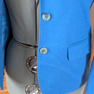 May include: A bright blue blazer with two matching buttons and a pocket. The blazer is displayed on a black dress form. The interior lining of the blazer is a lighter shade of blue.