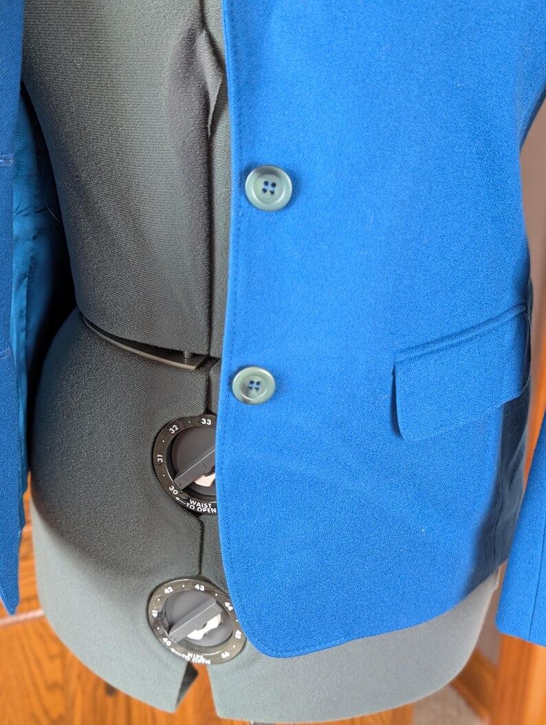 May include: A bright blue blazer with two matching buttons and a pocket. The blazer is displayed on a black dress form. The interior lining of the blazer is a lighter shade of blue.