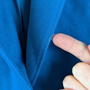 May include: Close-up of a vibrant blue blazer. The image highlights the fabric's texture and the tailored seams. A hand gently touches the material, showcasing the garment's quality and color.