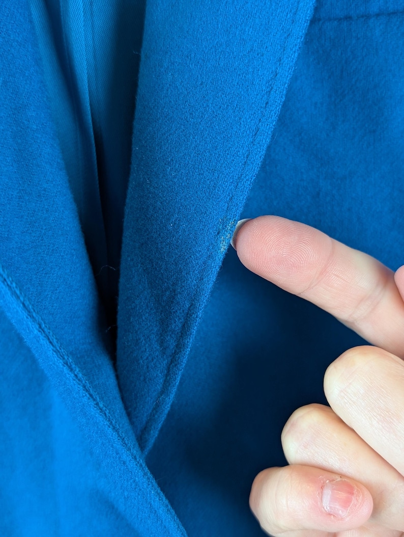 May include: Close-up of a vibrant blue blazer. The image highlights the fabric's texture and the tailored seams. A hand gently touches the material, showcasing the garment's quality and color.
