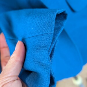 May include: Close-up of a bright blue blazer sleeve. The fabric is a solid color with a textured appearance. The sleeve is folded, revealing the interior lining. A button is visible in the background.