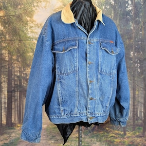 May include: A vintage blue denim jacket with a tan corduroy collar. The jacket has button closures, two chest pockets, and two side pockets. The jacket is displayed on a black mannequin.