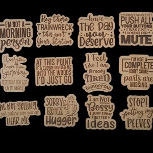 Puede incluir: Una colecci&oacute;n de recortes de madera con varias frases y citas humor&iacute;sticas. Las frases incluyen "I'm not a morning person", "Hey there trainwreck" y "I love you more than yesterday". Los recortes son de color marr&oacute;n claro.