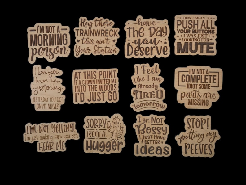 Puede incluir: Una colecci&oacute;n de recortes de madera con varias frases y citas humor&iacute;sticas. Las frases incluyen "I'm not a morning person", "Hey there trainwreck" y "I love you more than yesterday". Los recortes son de color marr&oacute;n claro.
