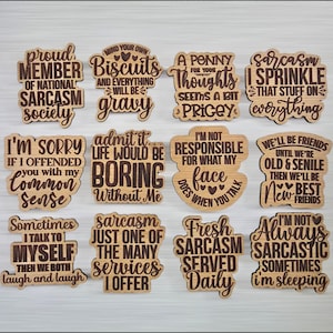 May include: A collection of twelve wooden plaques with humorous sayings in a variety of fonts. The plaques are light brown with dark brown text, featuring phrases like "Proud Member of National Sarcasm Society" and "Fresh Sarcasm Served Daily."