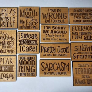 K&ouml;nnte beinhalten: Ein Satz von 10 Holzschildern mit humorvollen Spr&uuml;chen. Die Schilder sind alle rechteckig und haben eine hellbraune Holzoptik. Die Spr&uuml;che sind in schwarzen Lettern graviert. Einige der Spr&uuml;che beinhalten "Ich bin nur ein Strahl sarcastischen Sonnenscheins", "Ich schw&ouml;re, weil ich es tue", "Ich korrigiere deine Grammatik stillschweigend", und "Das ist eine schreckliche Idee, wann?"