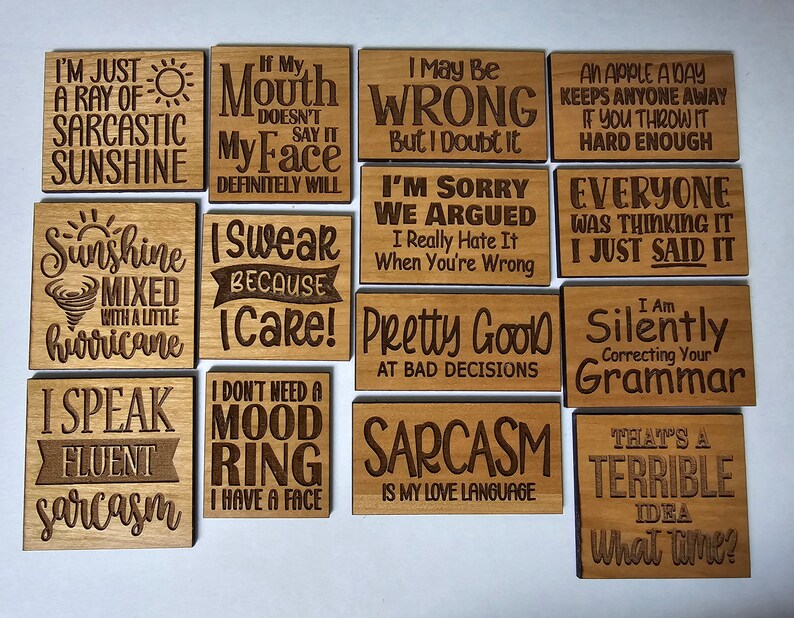K&ouml;nnte beinhalten: Ein Satz von 10 Holzschildern mit humorvollen Spr&uuml;chen. Die Schilder sind alle rechteckig und haben eine hellbraune Holzoptik. Die Spr&uuml;che sind in schwarzen Lettern graviert. Einige der Spr&uuml;che beinhalten "Ich bin nur ein Strahl sarcastischen Sonnenscheins", "Ich schw&ouml;re, weil ich es tue", "Ich korrigiere deine Grammatik stillschweigend", und "Das ist eine schreckliche Idee, wann?"