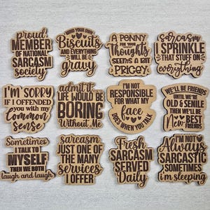 May include: A collection of twelve wooden plaques with humorous quotes and sayings, such as "Proud Member of National Sarcasm Society" and "Fresh Sarcasm Served Daily." The plaques are light brown with dark brown text.