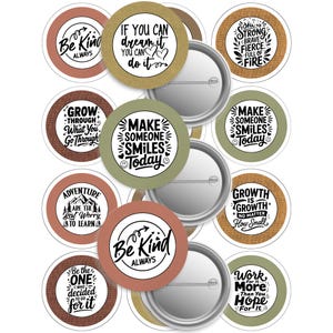 Può includere: Una collezione di spille rotonde con citazioni ispiratrici in bianco e nero su sfondi colorati. Le spille includono frasi come "Be Kind Always" e "Make Someone Smiles Today."