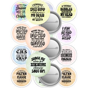 May include: A selection of round pin badges featuring witty sayings in black text on vibrant backgrounds. The badges have a metal back and a safety pin fastening. The phrases include "Judge me when you pay my bills otherwise shut up!"