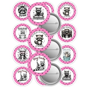 May include: A collection of round, pink and white buttons featuring raccoon illustrations. The buttons have various phrases like "Cute But Feral", "Booktrovert", and "Stay Trashy". The buttons are decorated with black polka dots.