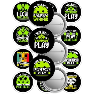 May include: A collection of black and white pickleball-themed buttons with various phrases and graphics. The buttons feature text like "I Love Pickleball," "Live Love Play," and "Pickleball is My Game." The buttons are round and have a pin backing.